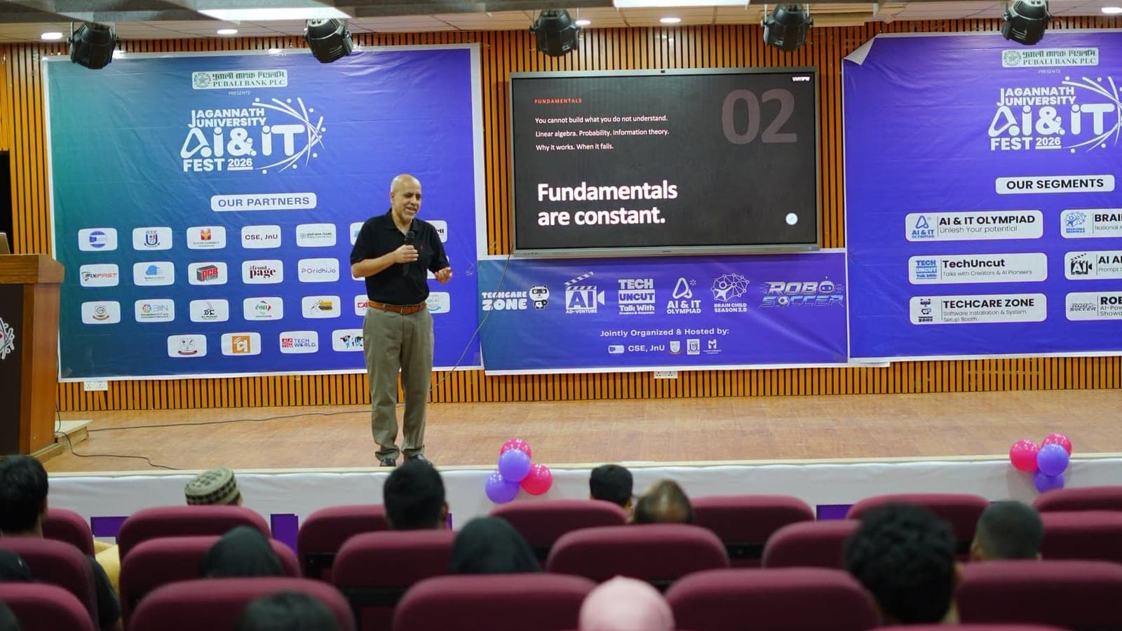 Dr. Zunaid Kazi delivering the opening keynote at the Jagannath University AI & IT Fest 2026, microphone in hand, beside a slide reading “Fundamentals are constant.”